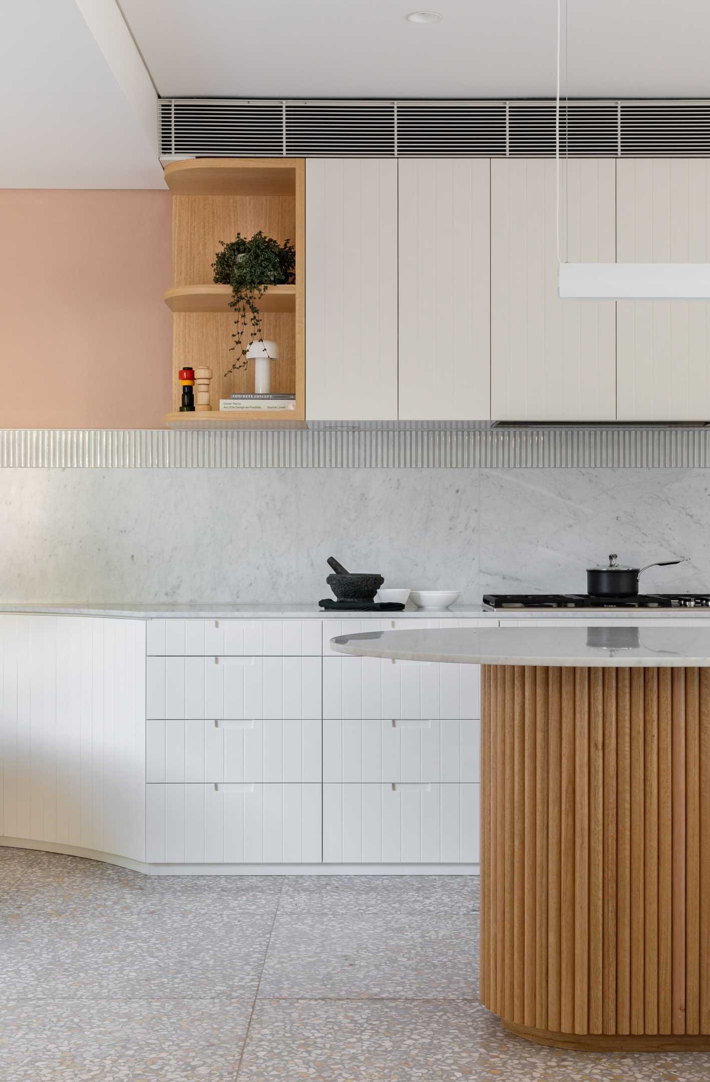 In this modern kitchen, the island features a hand-crafted with a scalloped timber base, topped with marble, holding court like those that sit around the island might.