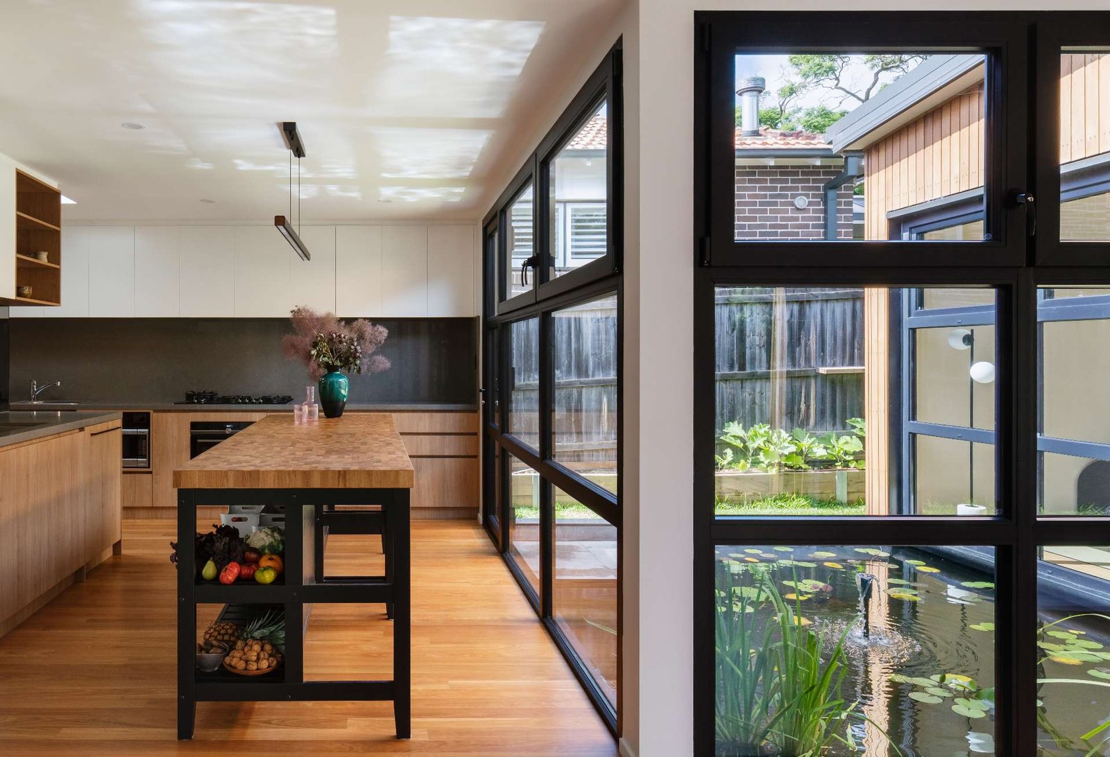 This Japanese-inspired kitchen has views of a tranquil reflection pond, blending natural textures with clean, modern lines. Black-framed windows flood the space with light, while the butcher-block island adds warmth and artisanal character.