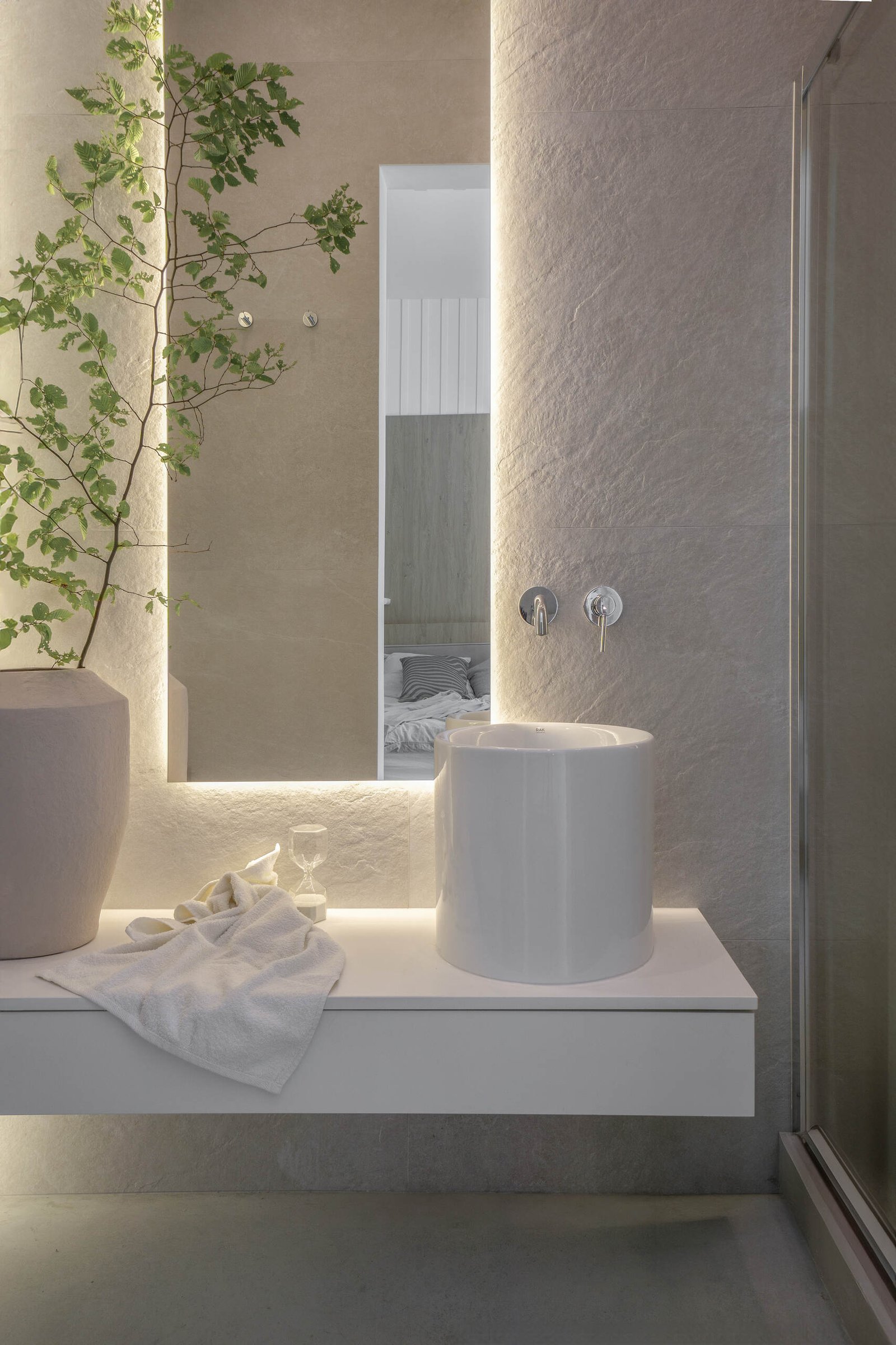 In an en-suite bathroom, a backlit mirror is positioned above the vanity, with the lighting highlighting the texture of the wall.