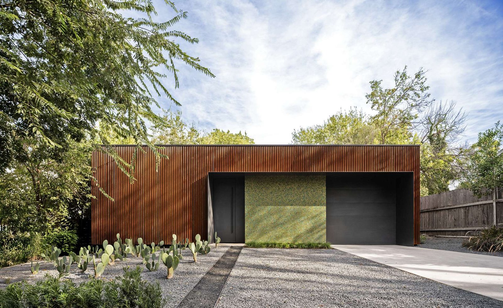 A bold mix of industrial and refined materials, this modern home pairs rusted corrugated steel with a shimmering mosaic wall for a striking first impression. The narrow window offers a glimpse into the tranquil, glass-lined interior.