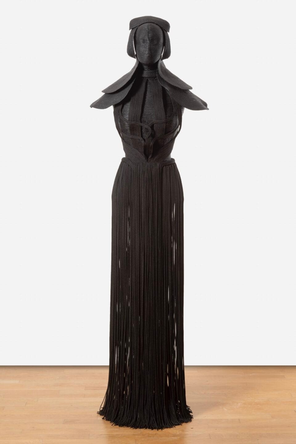 a sculpture made from black cord, thread, and metal in the form of a figure or long, dramatic garment
