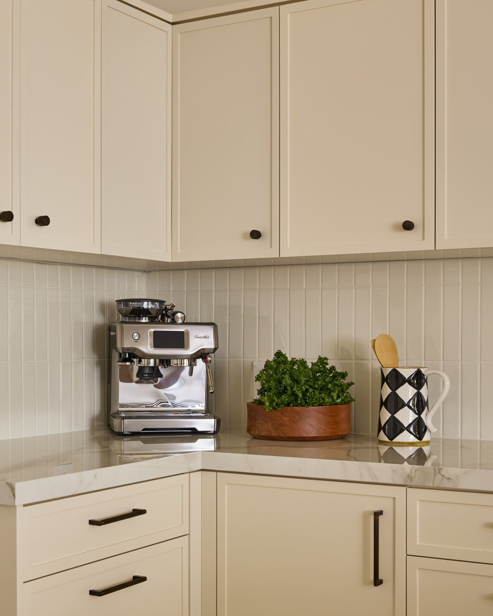 This updated kitchen manages to be both practical and picturesque. Creamy cabinetry is elevated by vertically stacked zellige tiles and dark bronze hardware, while a custom oak island topped with Dekton stone brings warmth and functionality. Brass and ceramic pendant lights overhead lend a vintage glow, and the whole space feels calm, considered, and deeply livable.