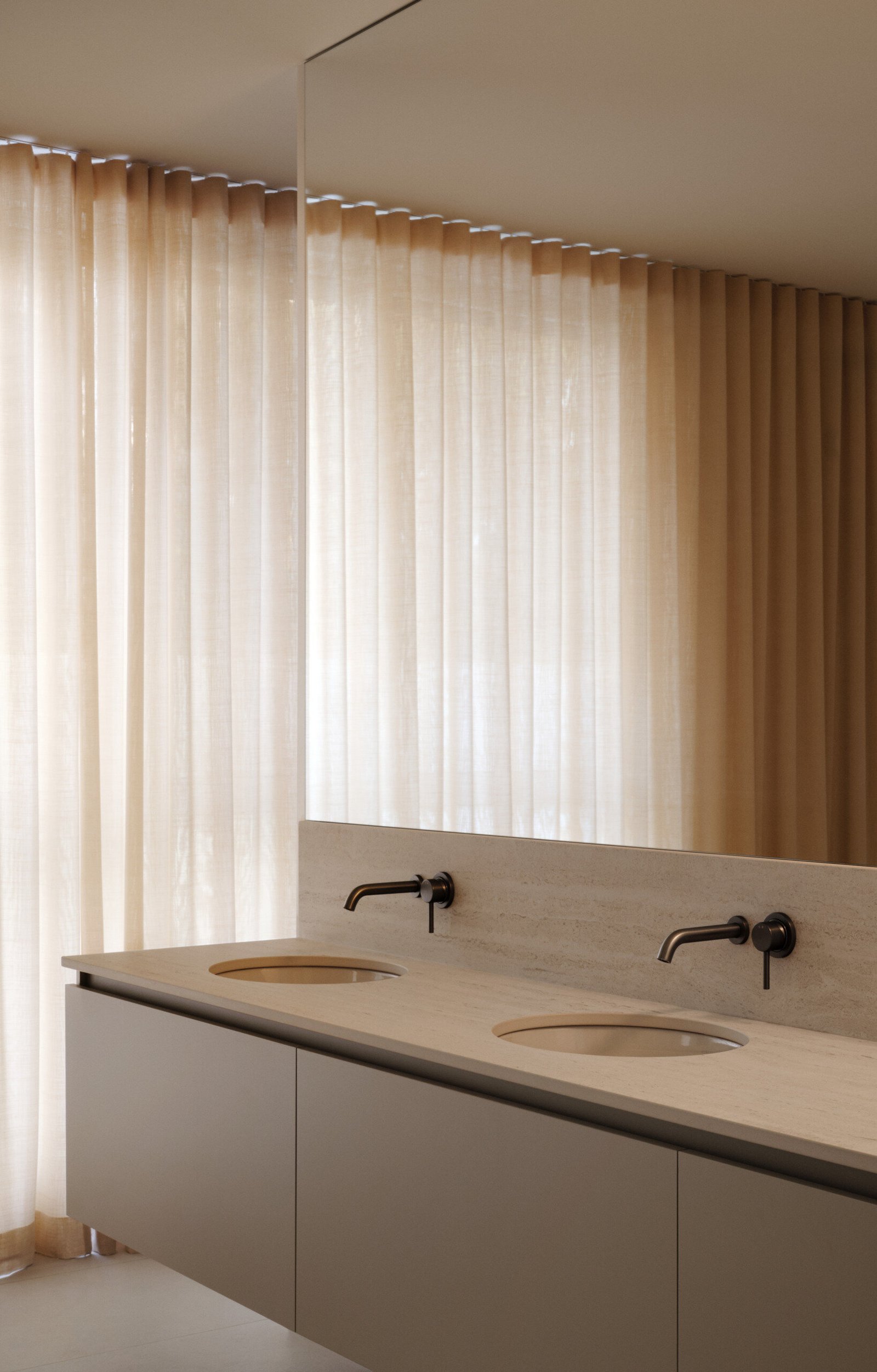 The primary bathroom is a quiet retreat, designed for comfort and calm. Sheer curtains filter soft light across a minimalist floating vanity with twin basins and a pale stone countertop. Muted metal fixtures add subtle contrast, while the mirrored above makes the room feel larger. With soothing tones, refined details, and no visual clutter, the ensuite feels spacious, tranquil, and perfectly suited for slow mornings. Two walk-in closets complete the suite with functional elegance.