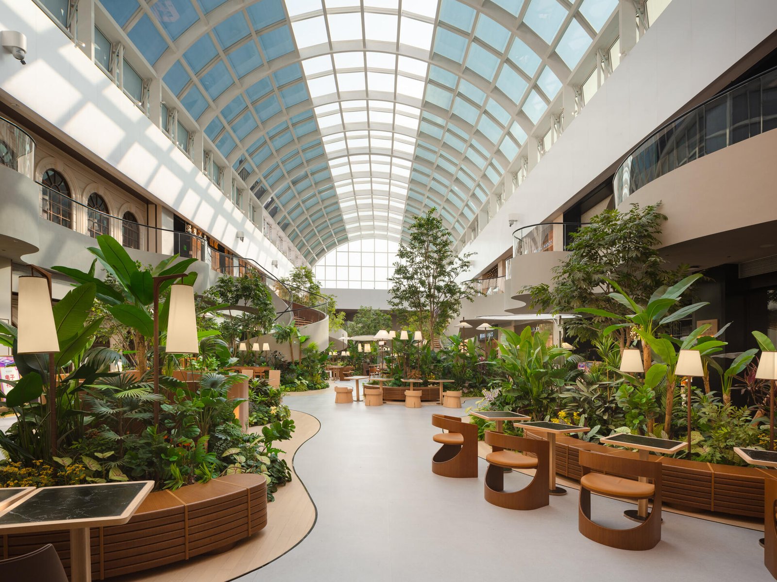A transparent arched skylight transforms this indoor public garden space with natural light. Steel curves echo leaf veins while shifting sun patterns on the floor mimic moss growing in a greenhouse. A calming, nature-inspired design moment.