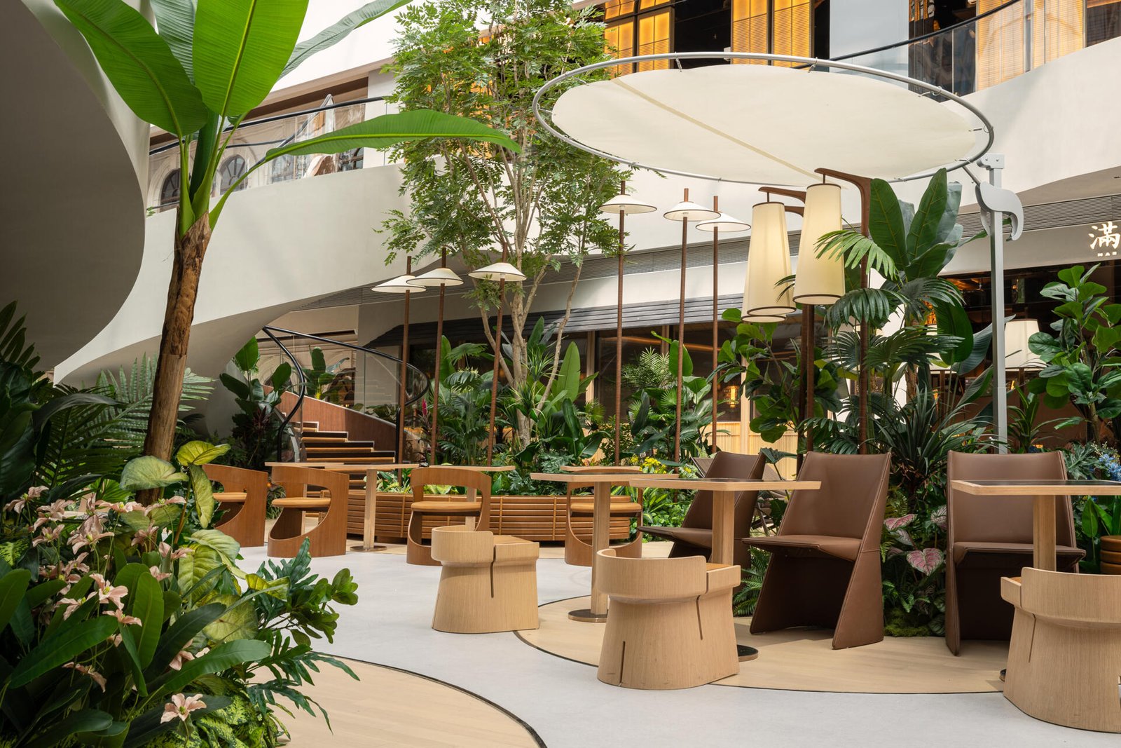 In this public plaza, long benches curve around clusters of greenery while sculptural chairs create relaxed, flexible seating. This dining space flows into a shared public garden, dissolving the line between restaurant and rest stop.