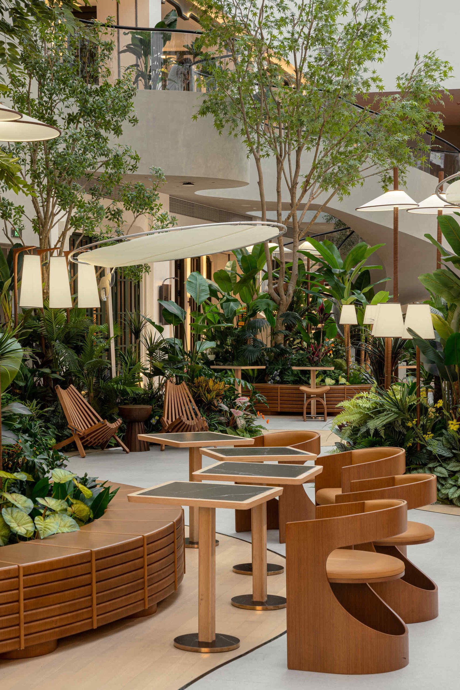 In this public plaza, long benches curve around clusters of greenery while sculptural chairs create relaxed, flexible seating. This dining space flows into a shared public garden, dissolving the line between restaurant and rest stop.