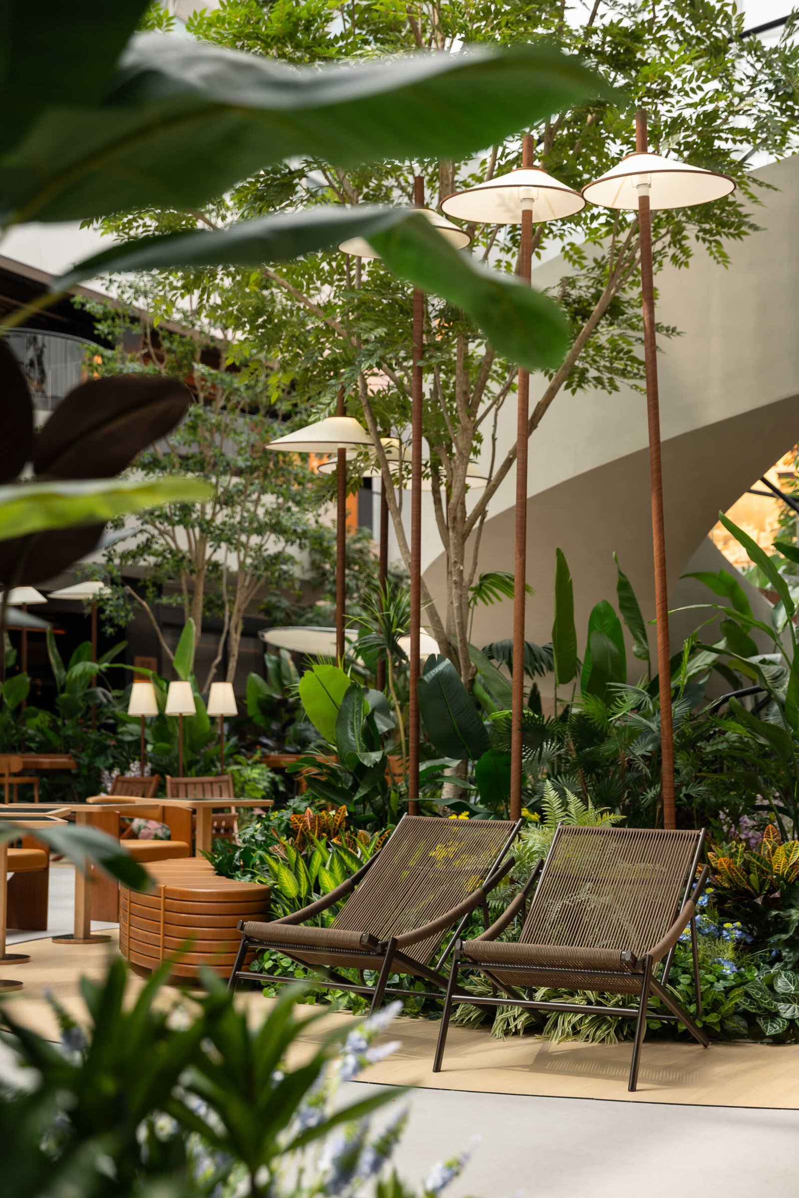 In this public plaza, long benches curve around clusters of greenery while sculptural chairs create relaxed, flexible seating. This dining space flows into a shared public garden, dissolving the line between restaurant and rest stop.