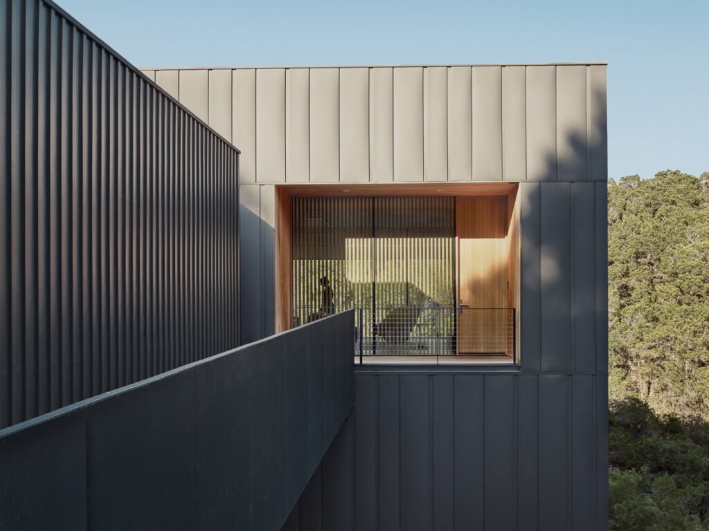 The exterior of this modern home is wrapped in vertical steel panels designed to weather, while deep wood-lined recesses frame curated views and allow light to shift throughout the day.