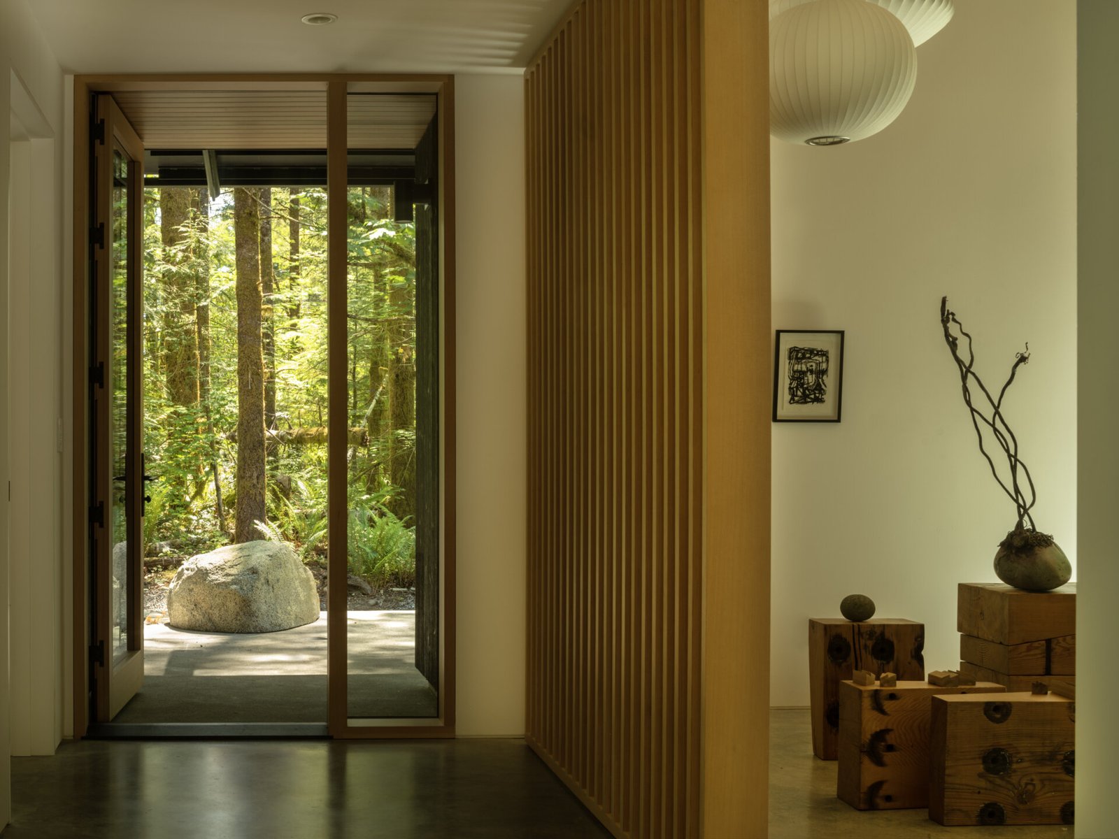 The entry blends natural textures with quiet modernity. A slatted wood screen adds privacy and rhythm, while stone and raw wood accents ground the space.