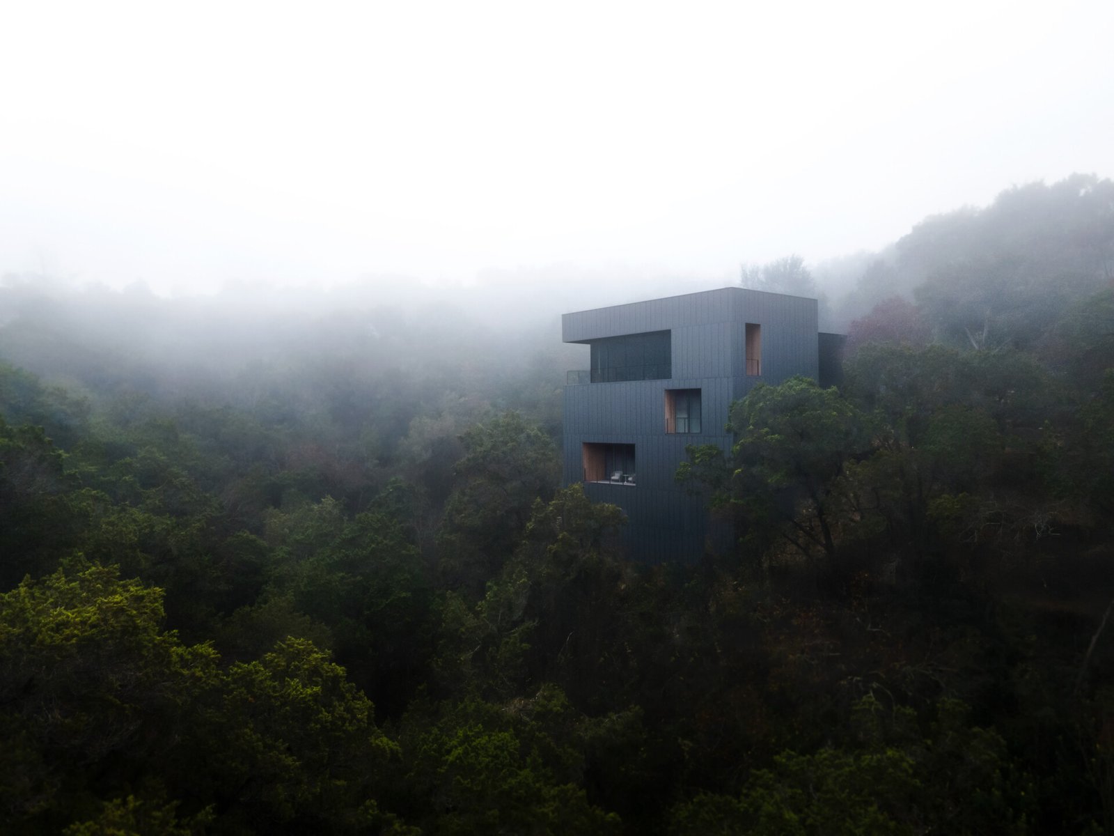 The exterior of this modern home is wrapped in vertical steel panels designed to weather, while deep wood-lined recesses frame curated views and allow light to shift throughout the day.