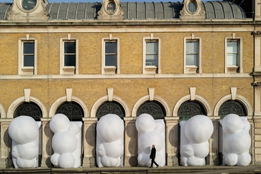 a series of large, white, bulbous, inflatable shapes designed by Steve Messam that stick out of an arched arcade on the first level of a brick building