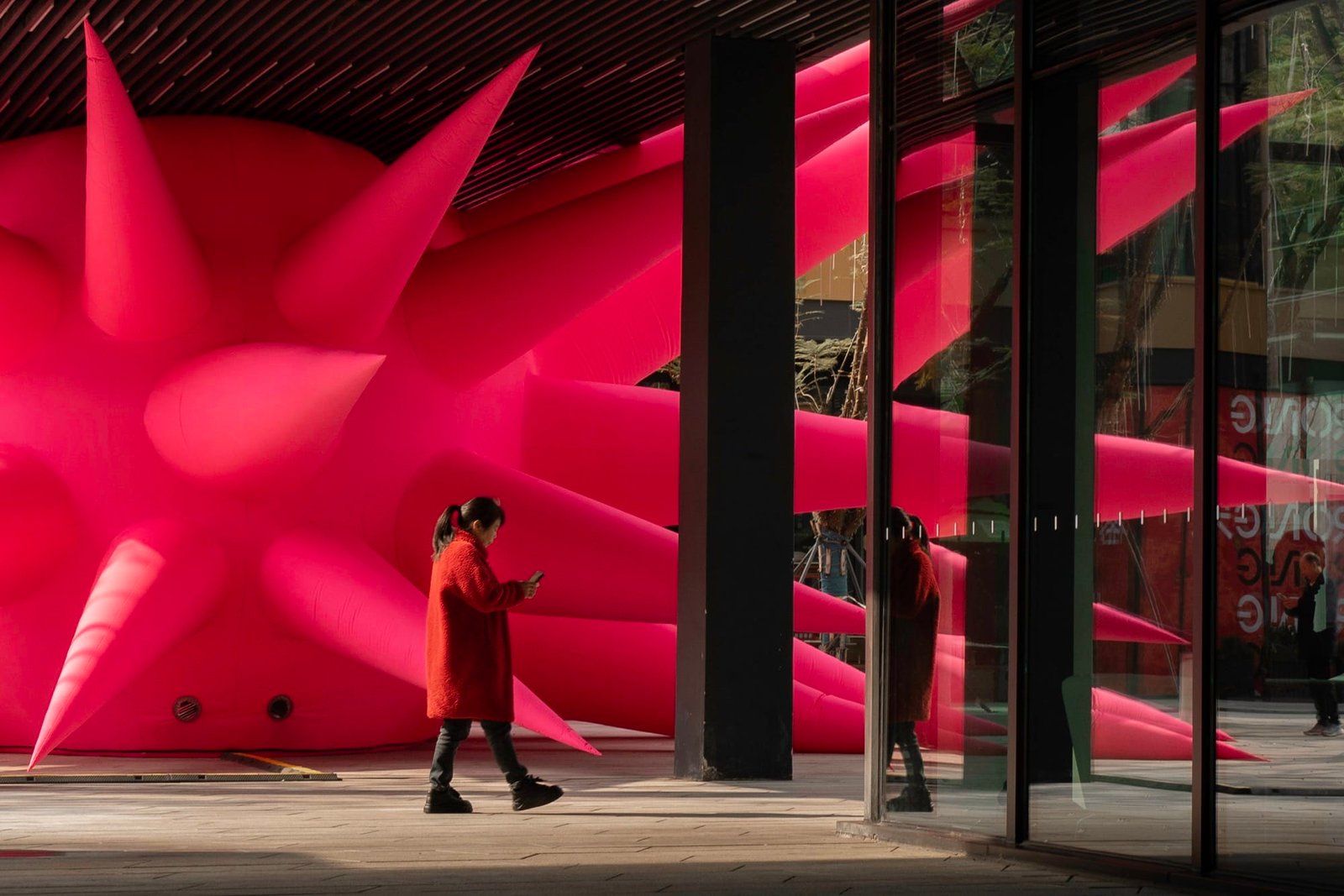 a woman walks in front of a large-scale inflatable sculpture installation by Steve Messam of ared, spiked form wedged under a bridge