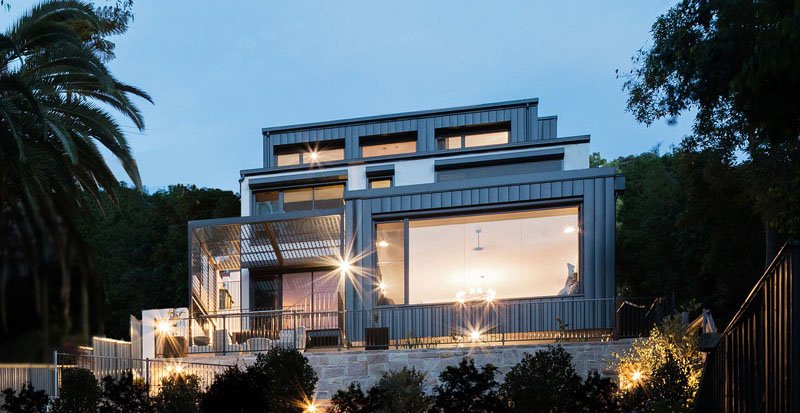 A contemporary home rises along a steep slope and blends seamlessly with the surrounding bushland. Built with fire-resistant materials and steel shutters for protection, the house balances safety with style, featuring multi-level living, expansive picture windows, and a strong connection between indoors and outdoors.