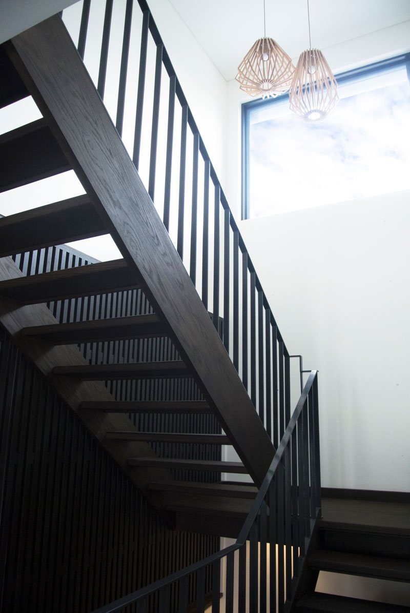 The dark wood staircase is both functional and sculptural, guiding movement through the house while framing bush views along the way. A large window alongside the stairs ensures every step is naturally lit.