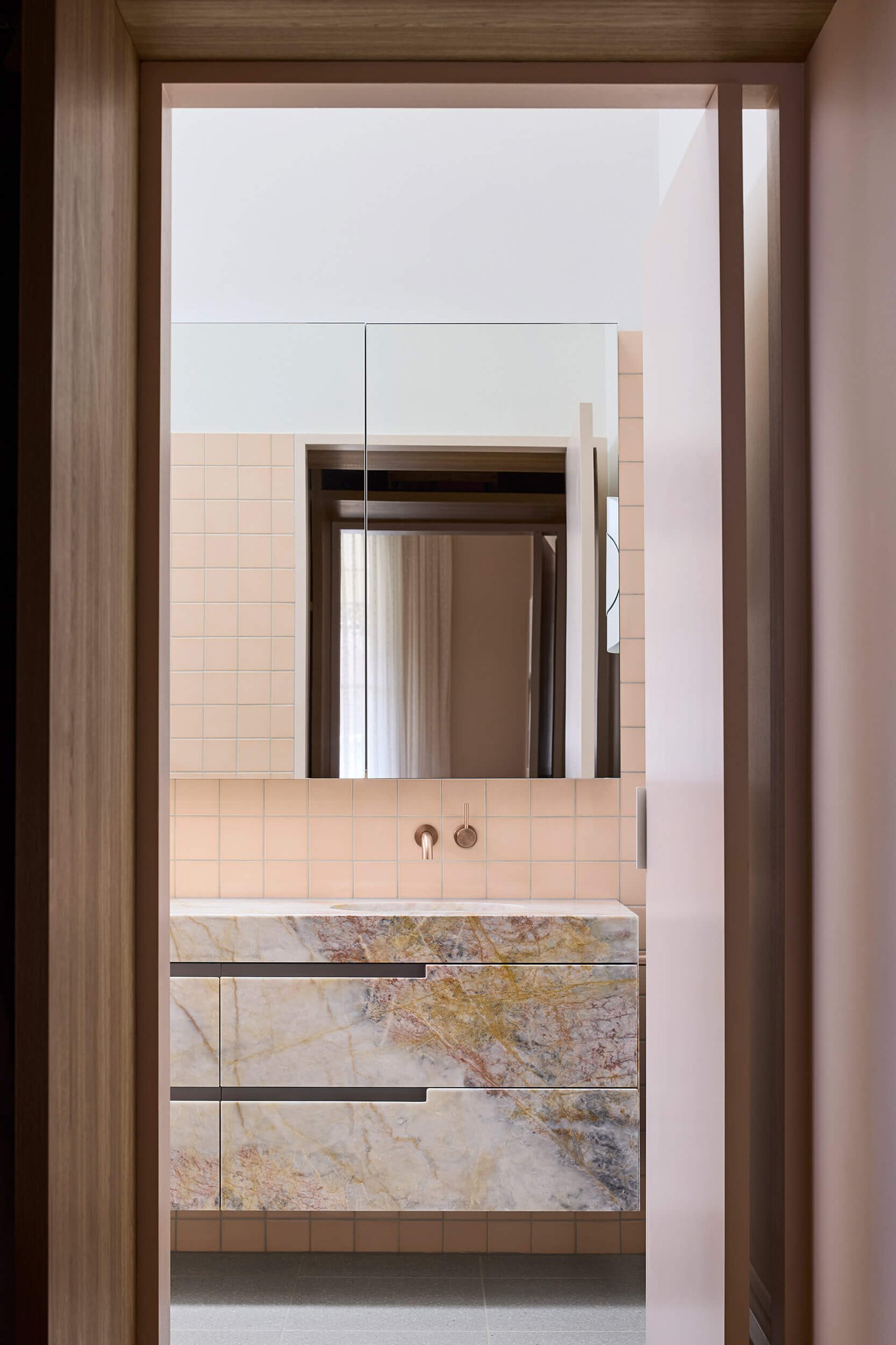 Australian marble with apricot and copper undertones carries through this ensuite bathroom, where color and texture build a sense of intimacy.