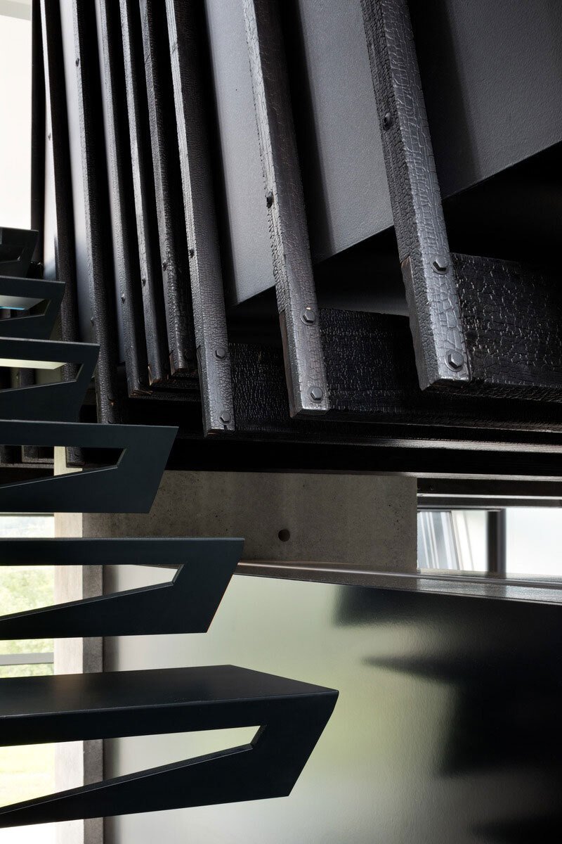 A black sculptural staircase leads to calm, light-filled bedrooms where Shou Sugi Ban details continue the home’s cohesive design.