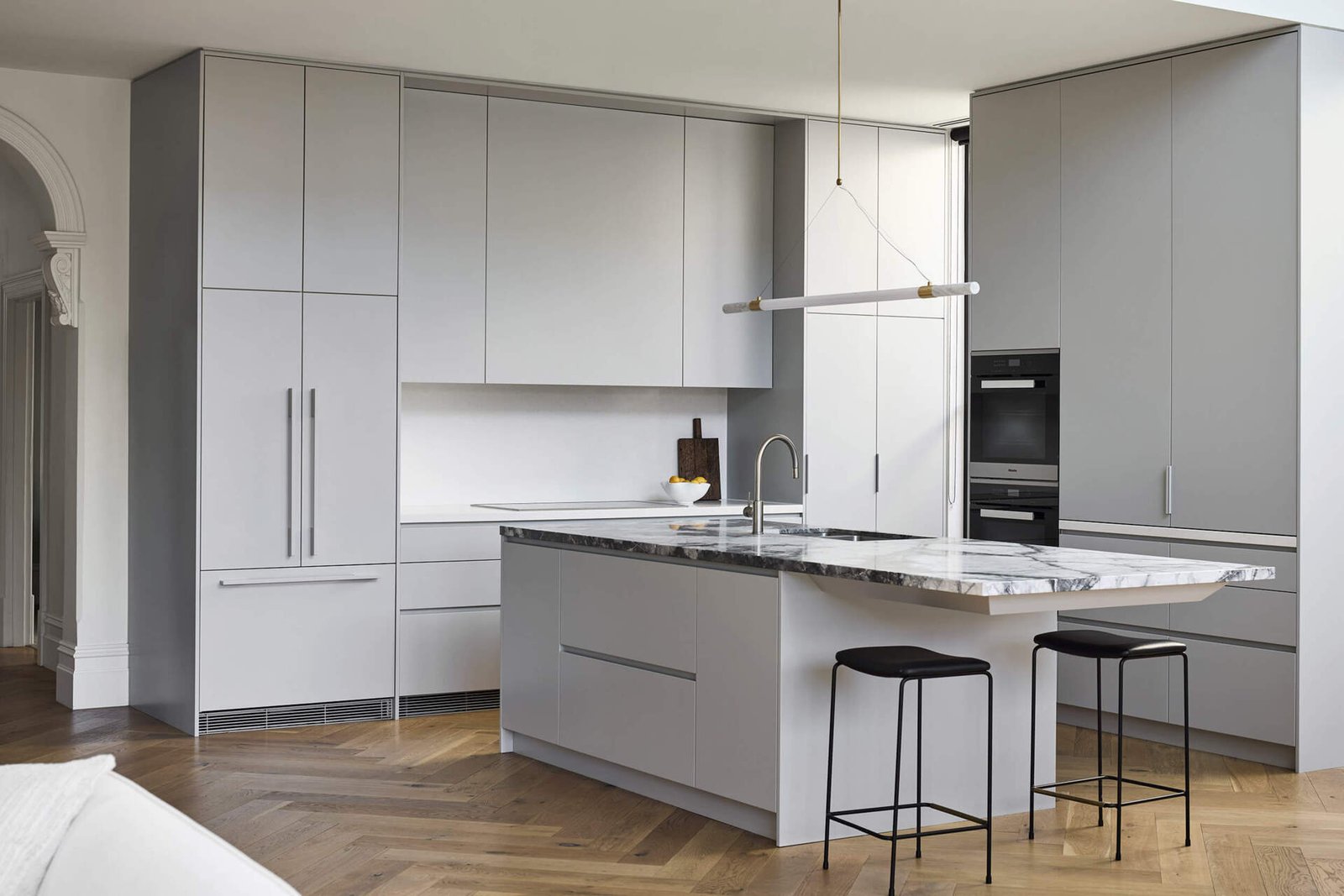 This kitchen centers on a cantilevered stone island that serves as both sculptural statement and family gathering point. Suspended lighting in brass and marble continues the refined aesthetic. Hidden appliances maintain a sense of calm order, reinforcing the balance of function and beauty.