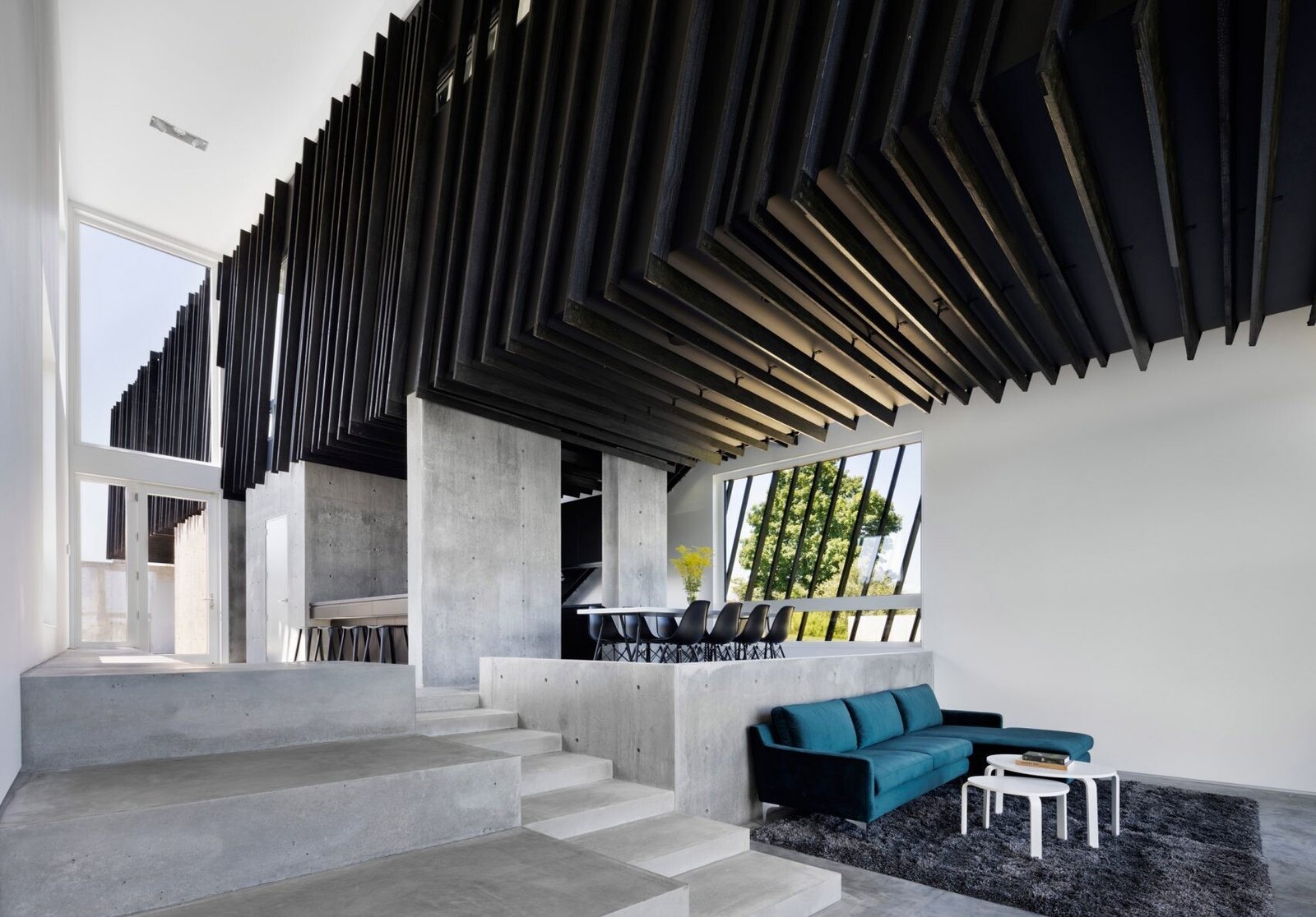 A bright blue couch and panoramic mountain views bring life and warmth to this minimalist living room framed by concrete and glass.