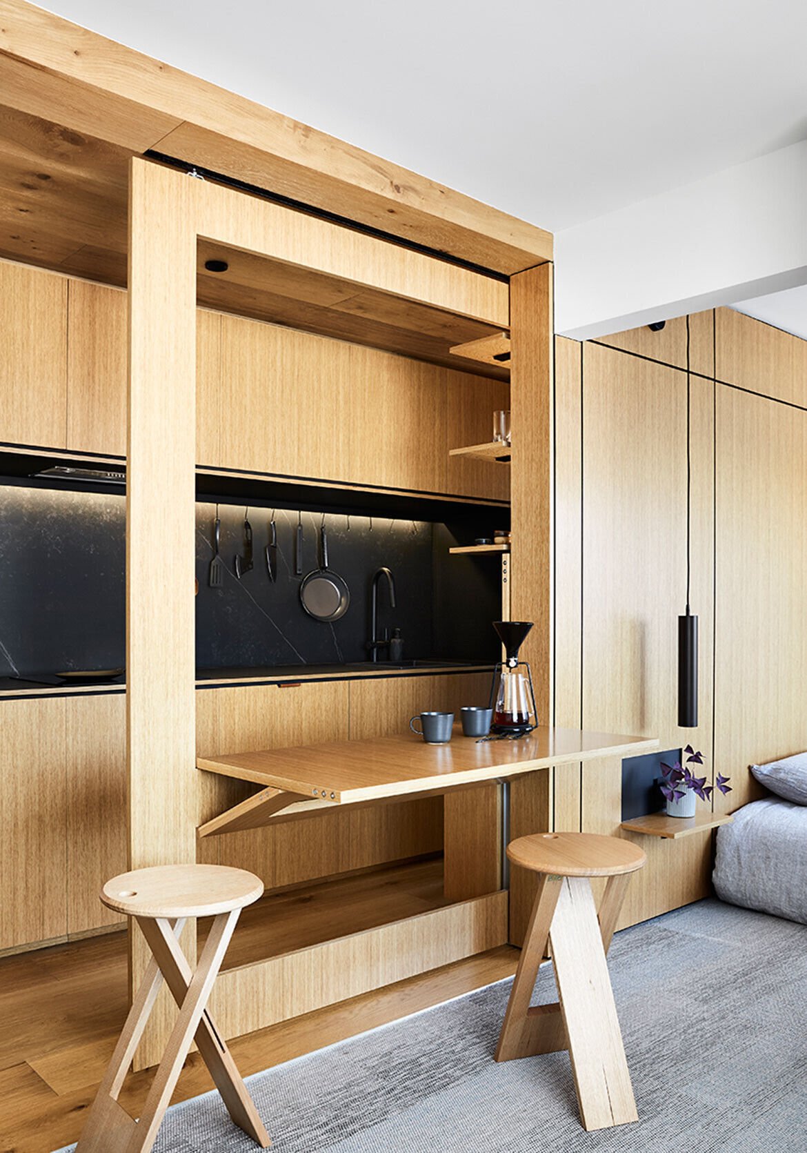 A fold-down dining table slides out from a hidden cavity, proving smart furniture can completely change how a small apartment functions.