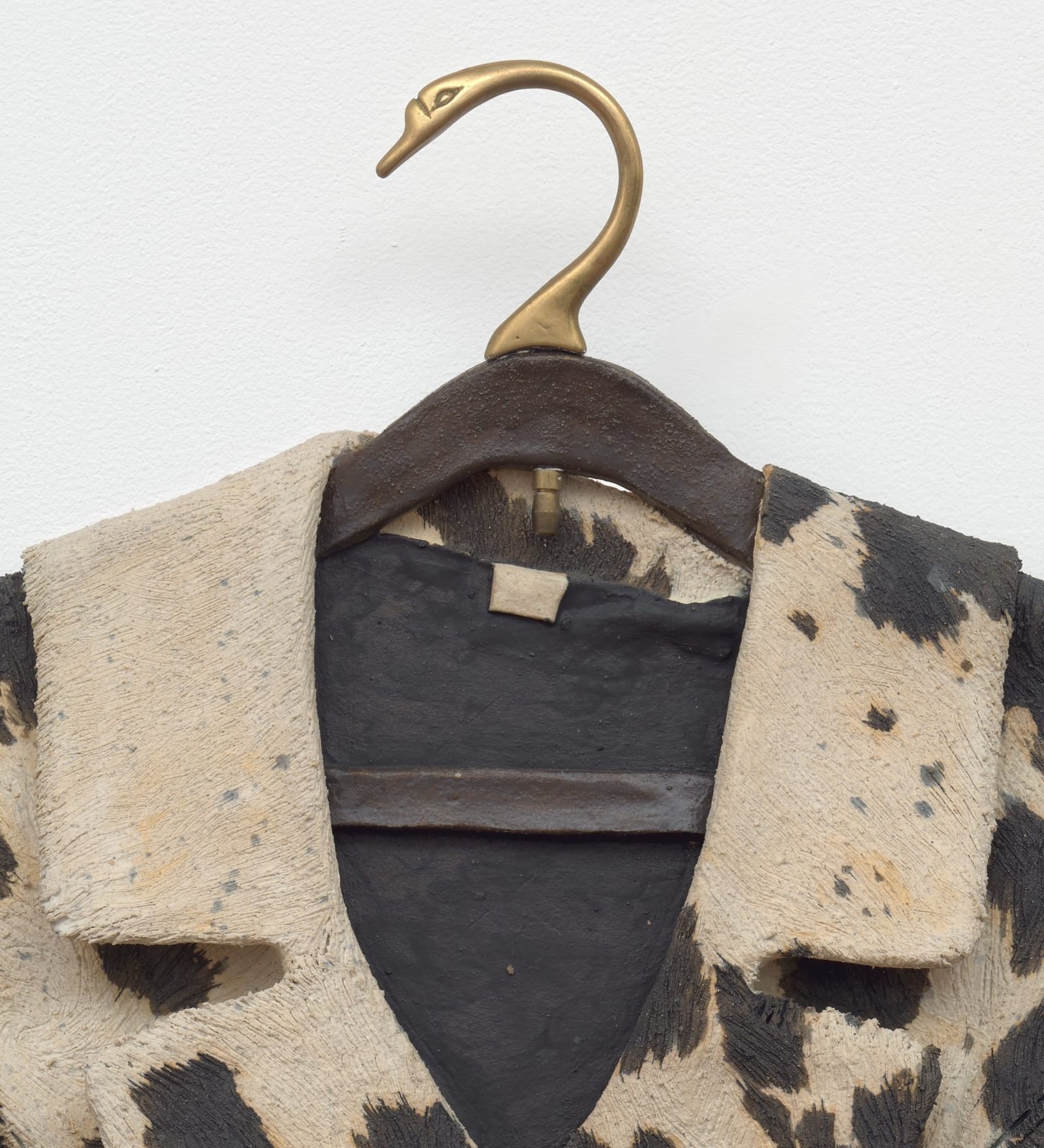 a detail of a ceramic sculpture by Stephanie Temma Heir featuring a cowprint jacket on a swan shaped hanger