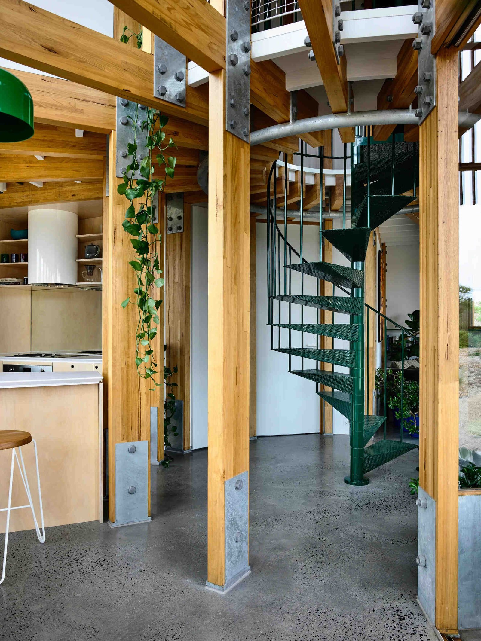 A dark green spiral staircase at the centre of a circular beach house interior.