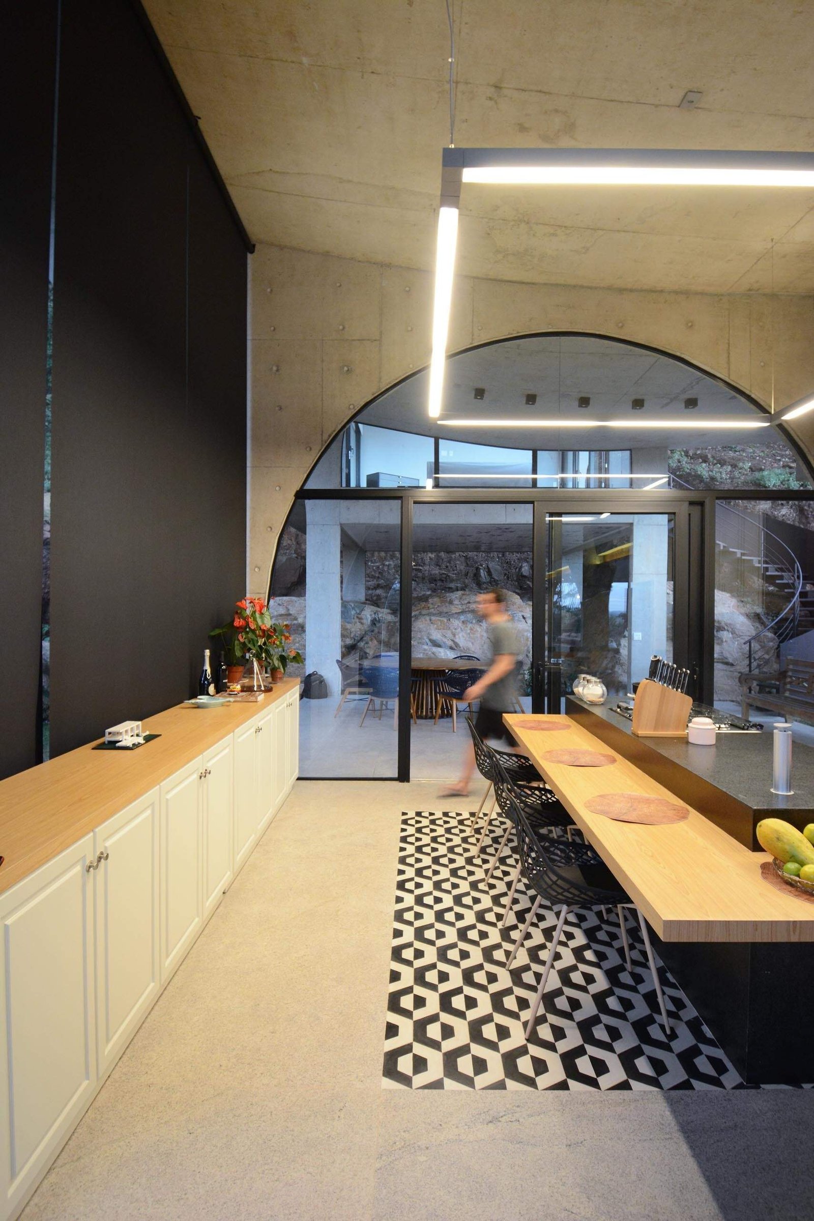 A long kitchen island anchors the social heart of the home while black framed windows follow the curves of the concrete arches above.