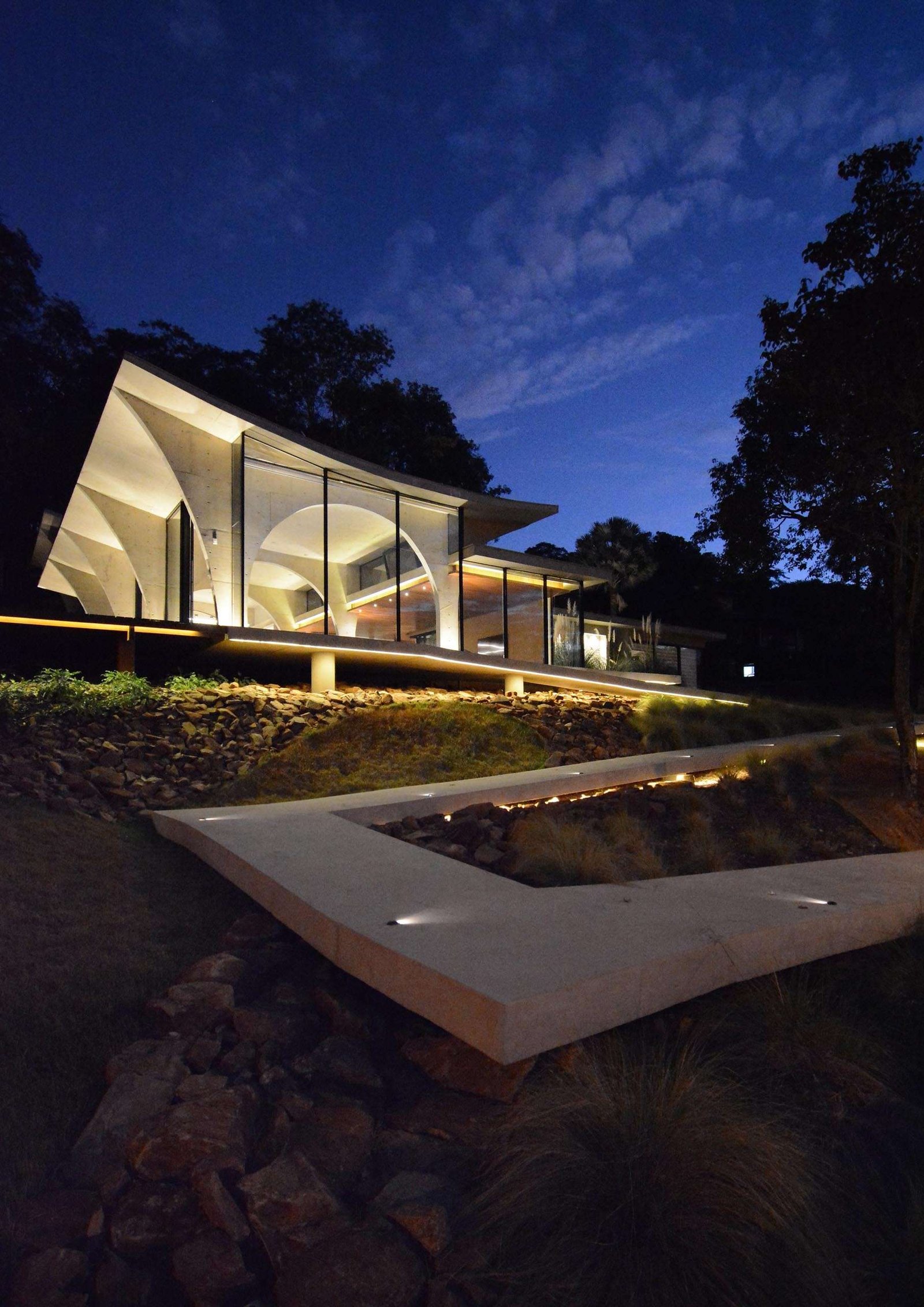 A winding concrete ramp leads up to Casa Joy in Brazil, revealing a sculptural modern home defined by six dramatic concrete arches and a concave roof overlooking the valley.