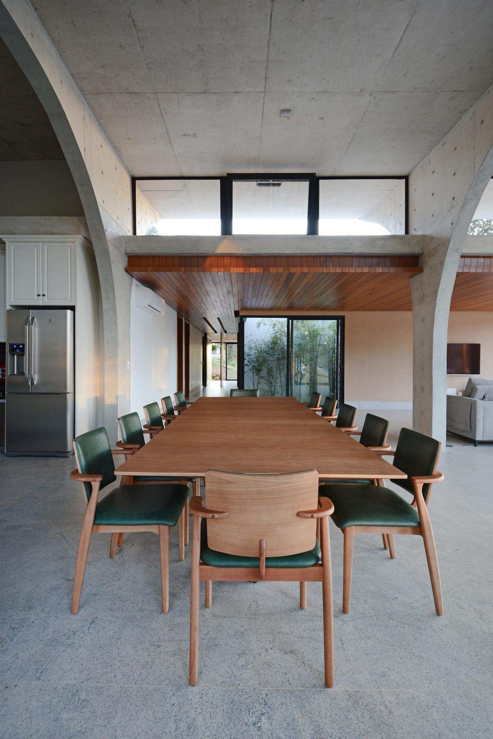 The living room, dining area, and kitchen share a dramatic double height space framed by concrete arches and large sliding glass doors that connect the interior to the gardens.