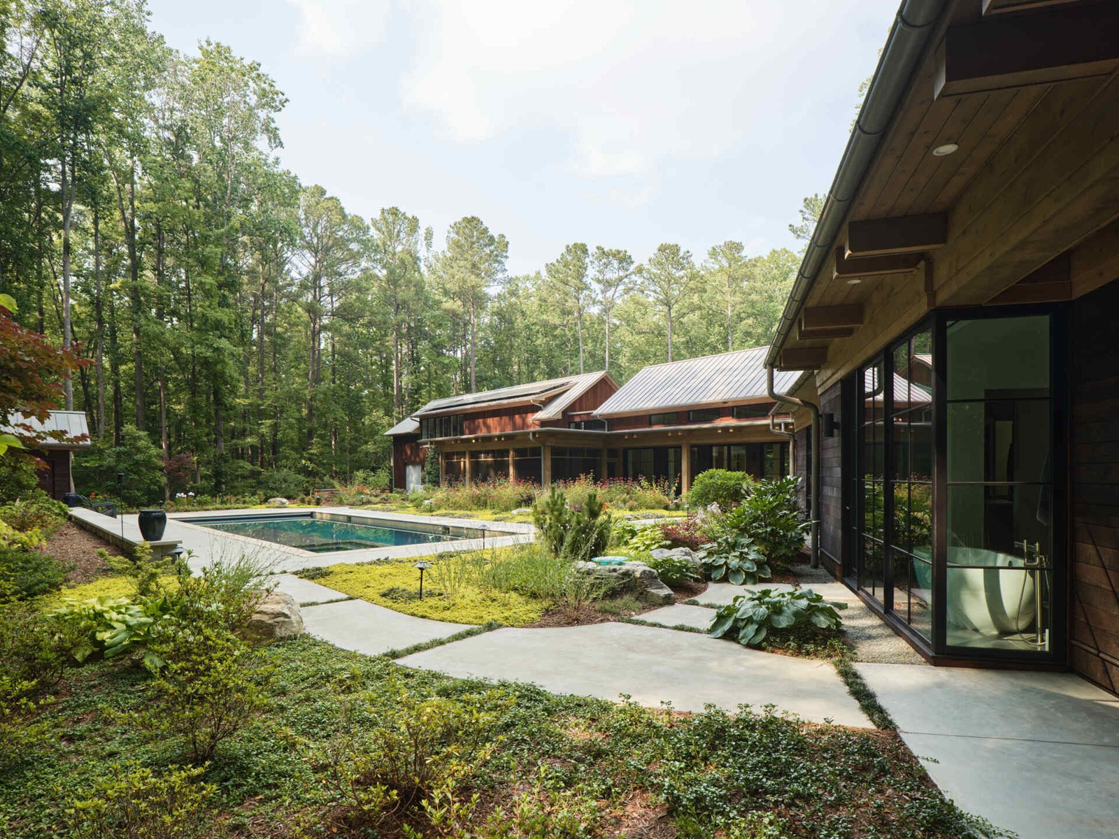 Double-height living, expansive windows, and a stone chimney define this warm, light-filled home in North Carolina, while an organized garden has room for a growing, relaxing, and enjoying the pool.