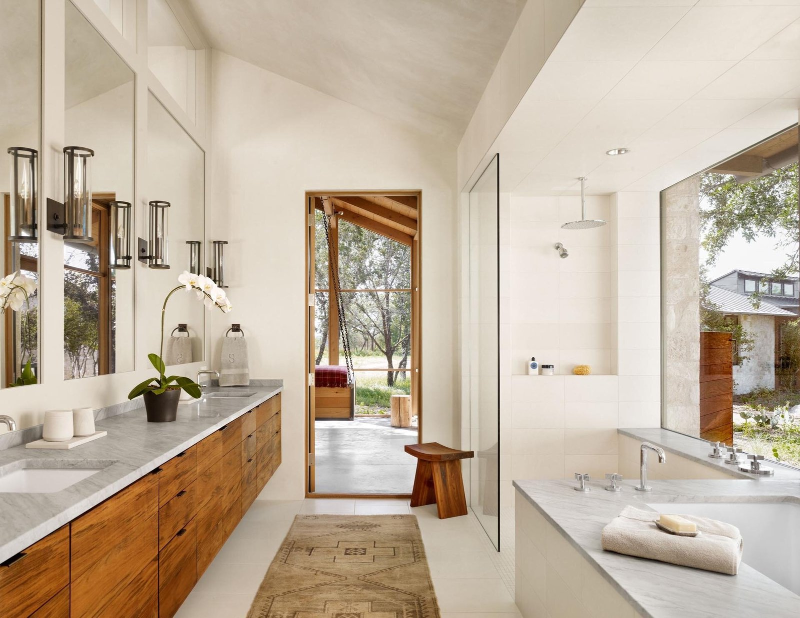 A primary suite with a vaulted ceiling, recessed bed, and a walk-through bathroom featuring a long wood vanity and built-in tub.