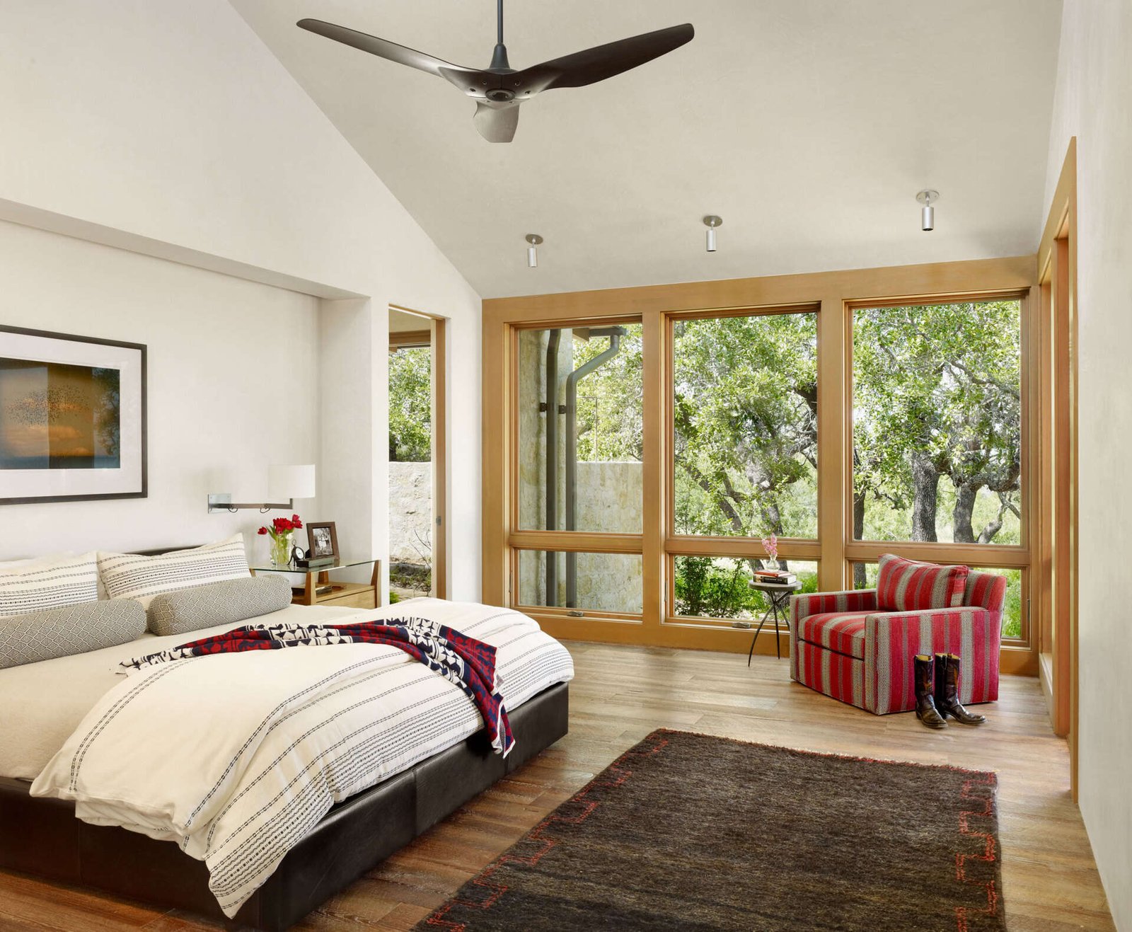 A primary suite with a vaulted ceiling, recessed bed, and a walk-through bathroom featuring a long wood vanity and built-in tub.