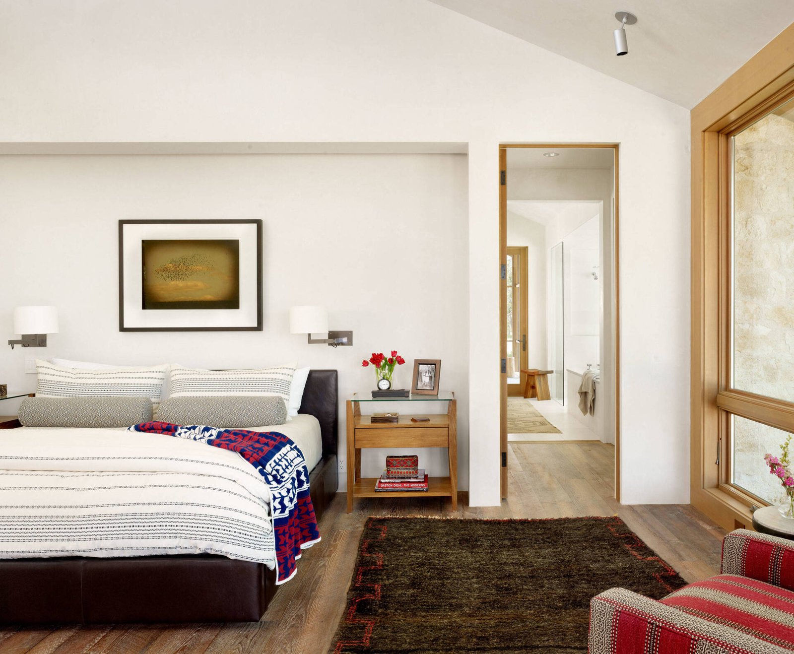 A primary suite with a vaulted ceiling, recessed bed, and a walk-through bathroom featuring a long wood vanity and built-in tub.