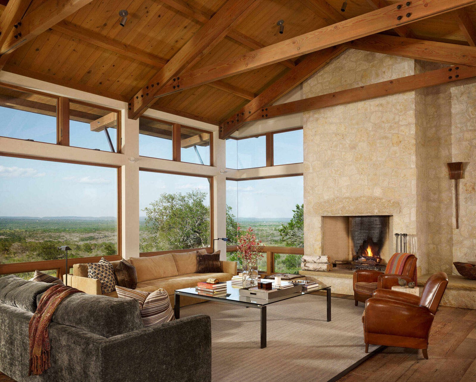 A living room where limestone walls meet exposed wood trusses, creating a warm and textured interior anchored by a stone fireplace.