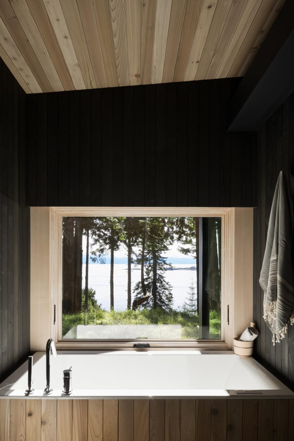 A modern bathroom with blackened wood walls and a built-in bathtub, continuing the cabin’s bold and minimal aesthetic.