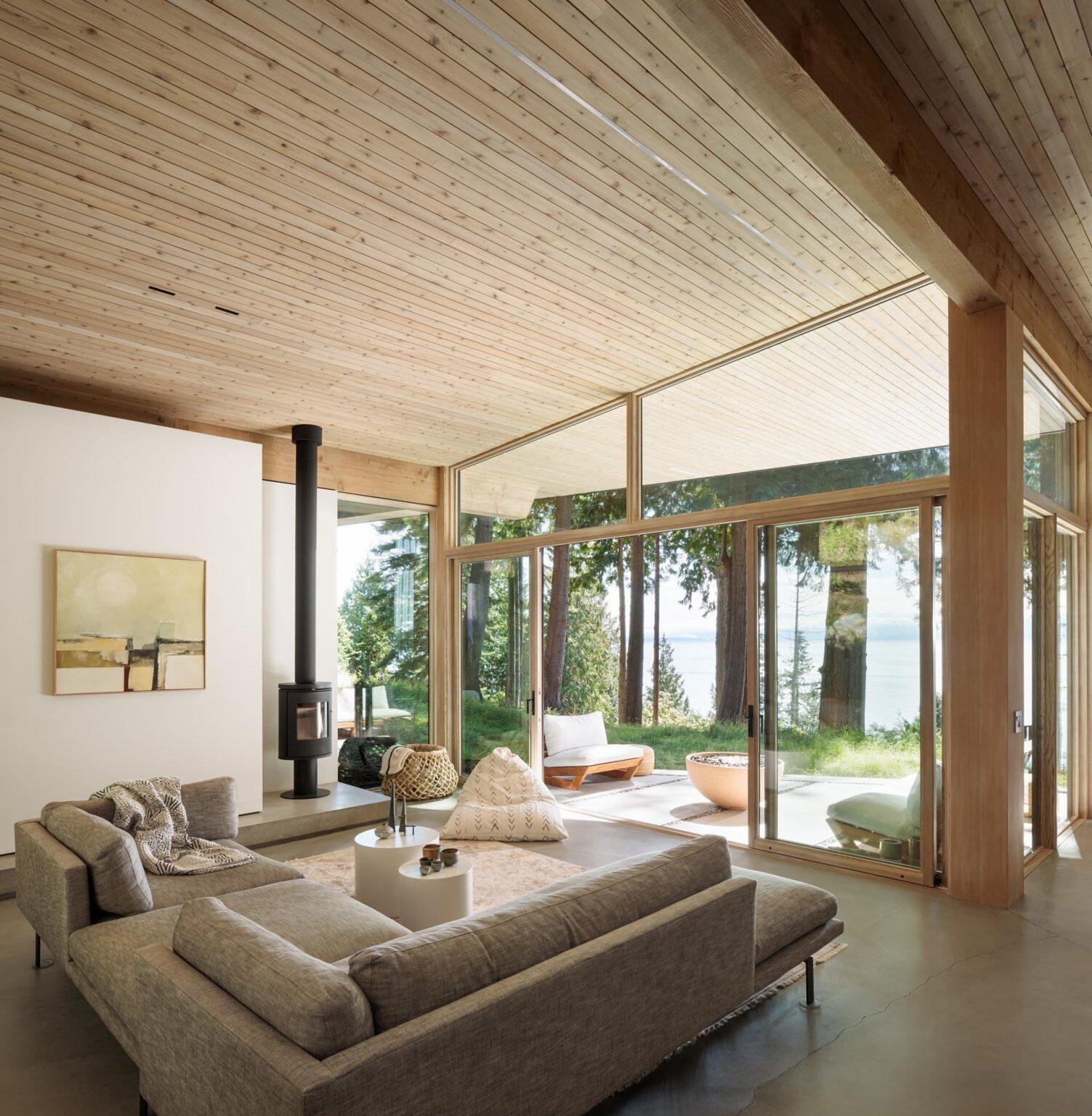 A minimalist living room with a gray sofa and black fireplace opens through sliding glass doors to a covered patio with water views.