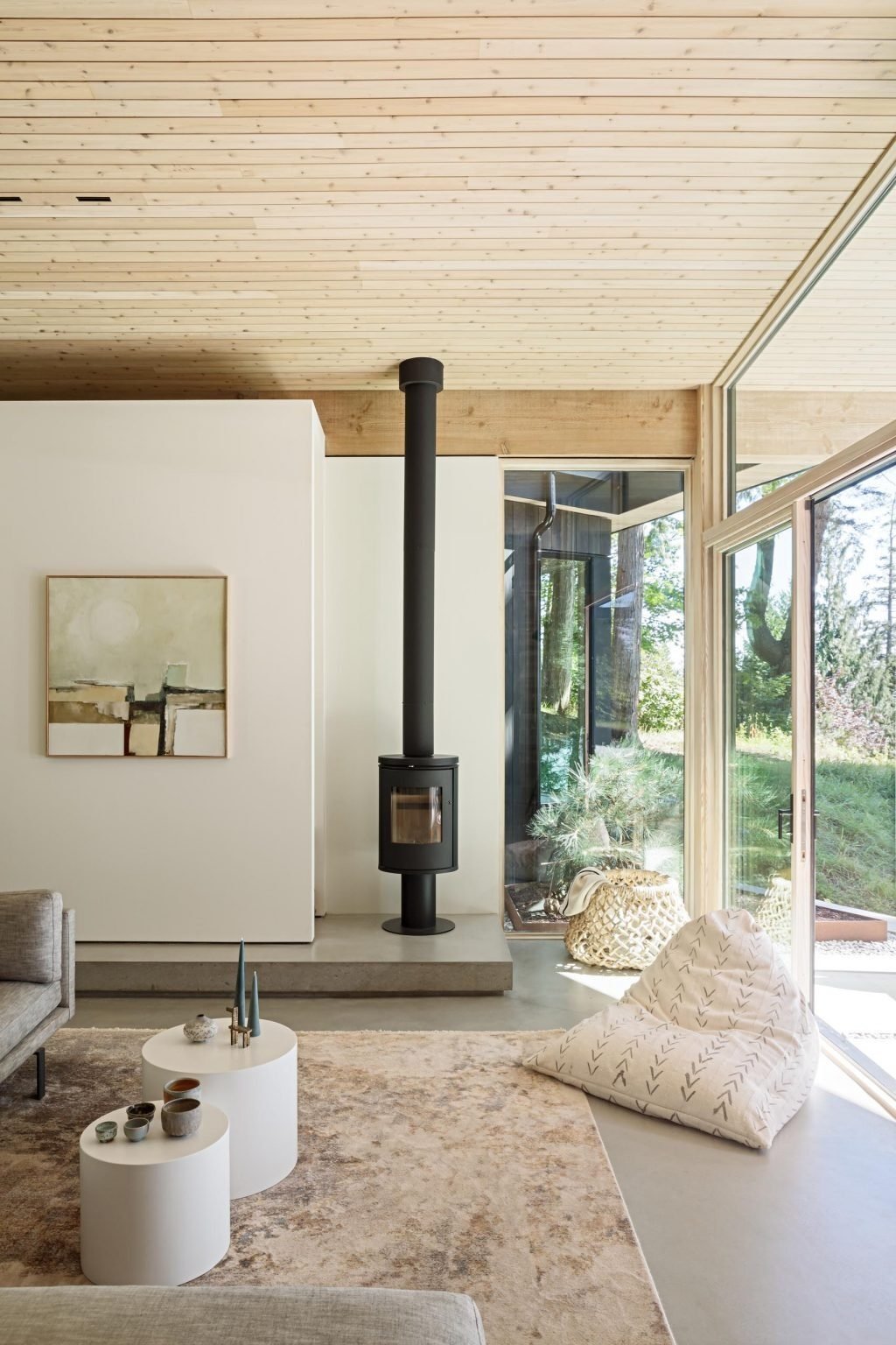 A minimalist living room with a gray sofa and black fireplace opens through sliding glass doors to a covered patio with water views.