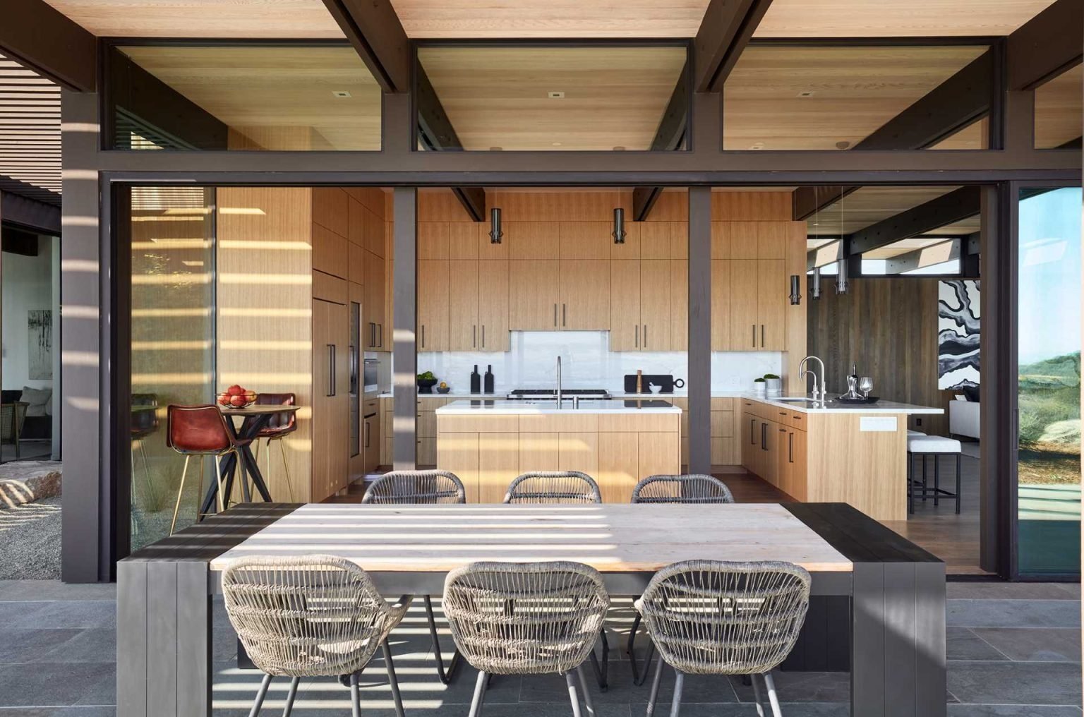 Large glass openings connect the interiors to an expansive covered patio designed for dining, lounging, and entertaining outdoors.