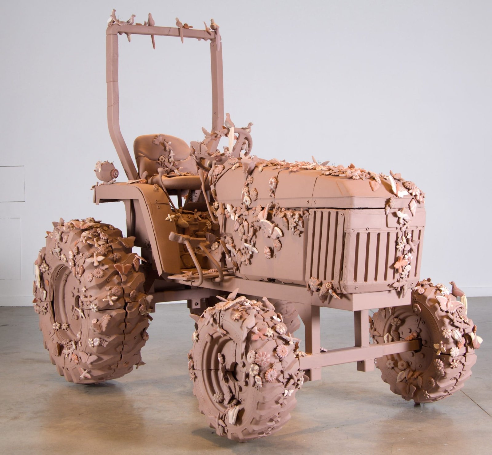 a sculpture of a John Deere tractor that is entirely pink with botanicals and birds all around it