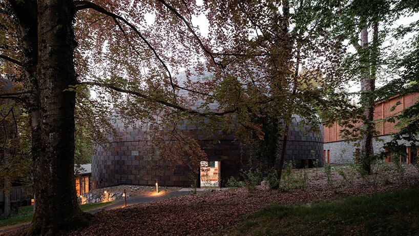 Low angle view of the curved copper music hall partially embedded into the forested hill